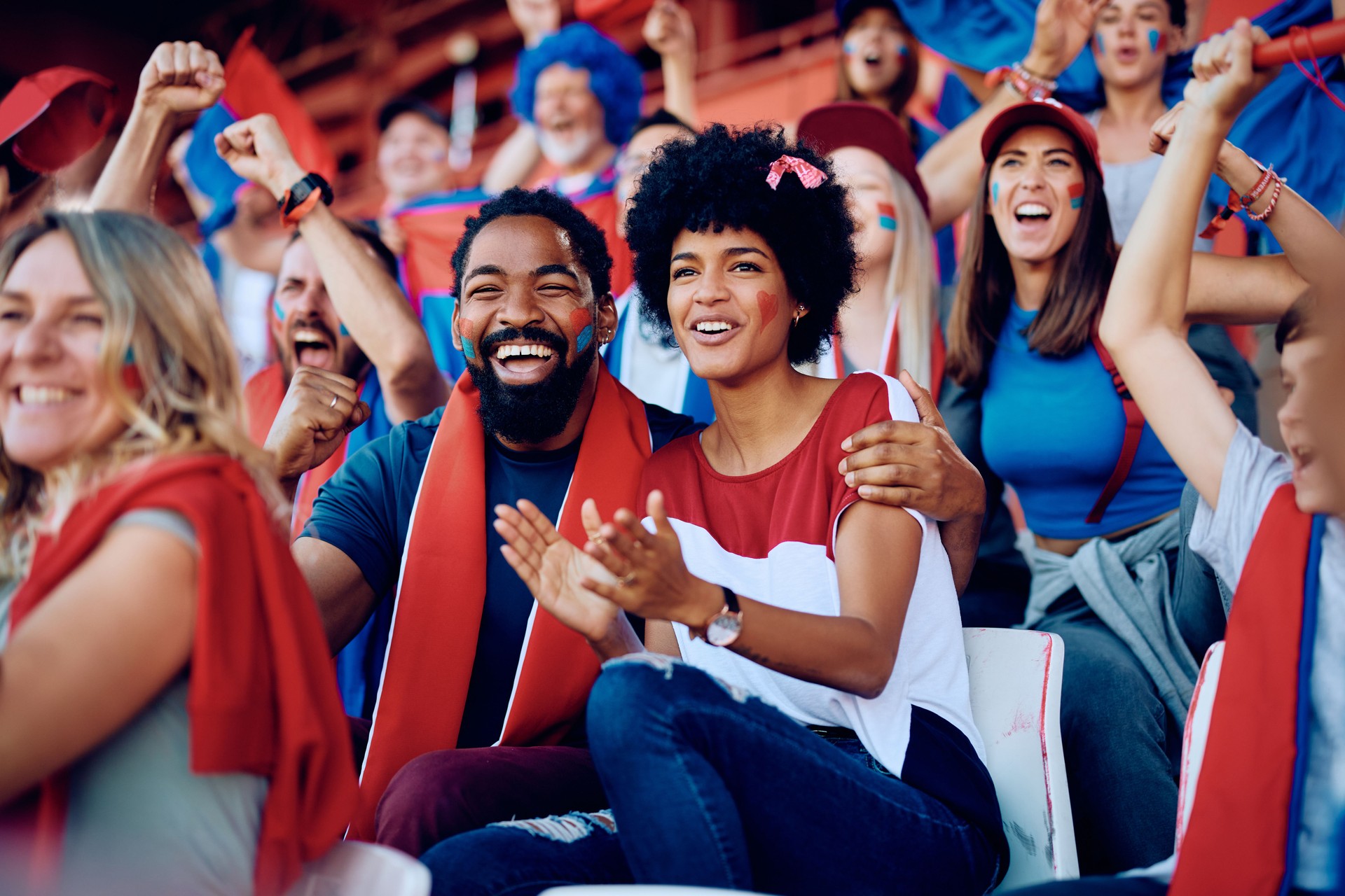 Happy black couple cheering while speciating a sports championship at the stadium.