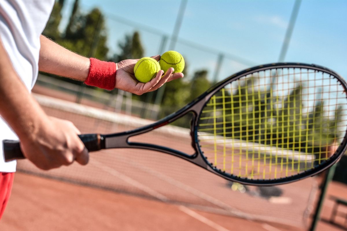 Close up photo of young man on tennis court. Man playing tennis. Man is ready to throw tennis ball. Beautiful forest area as background